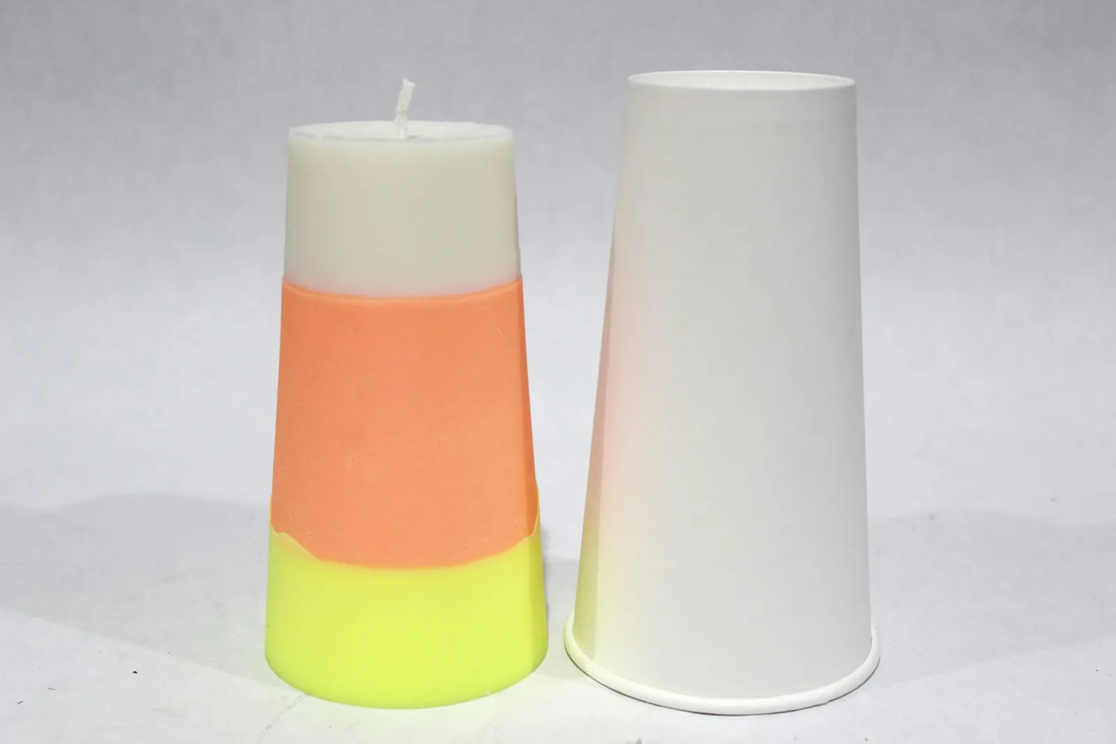 A striped DIY candy corn candle set next to a paper cup mold