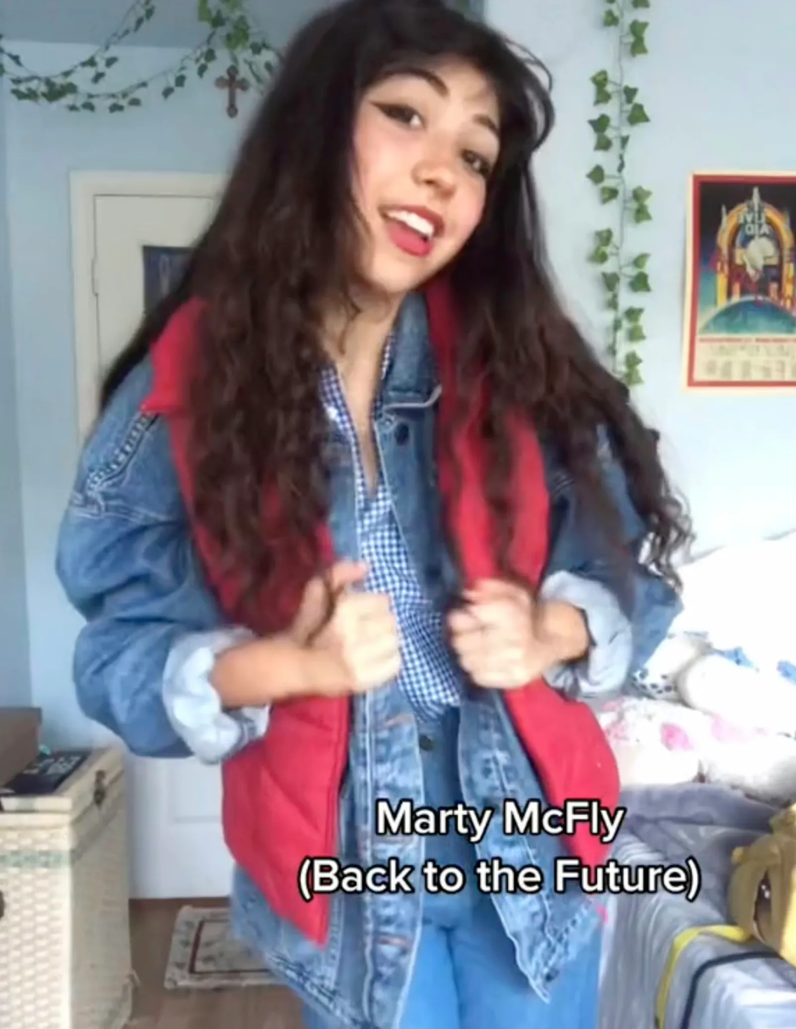 Woman with long dark hair wearing denim jacket under a red vest