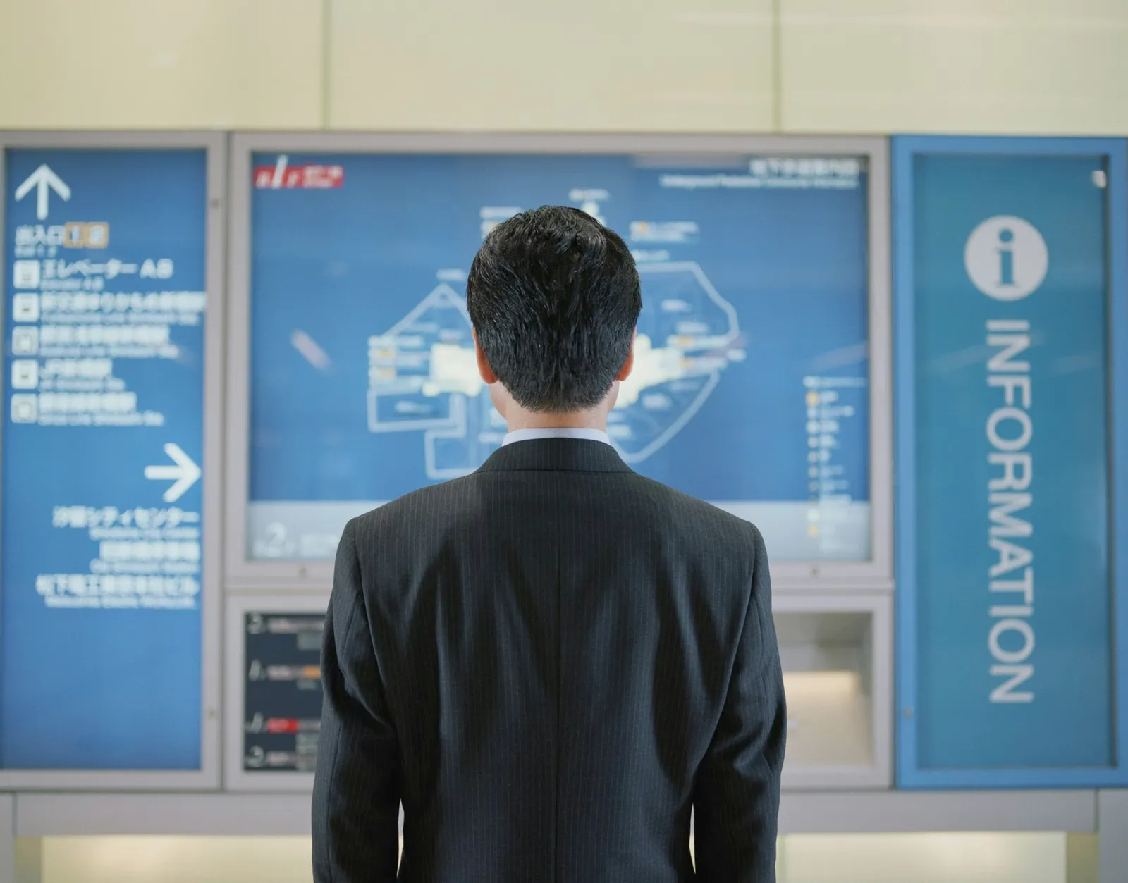 Mature businessman looking at map in subway station, rear view