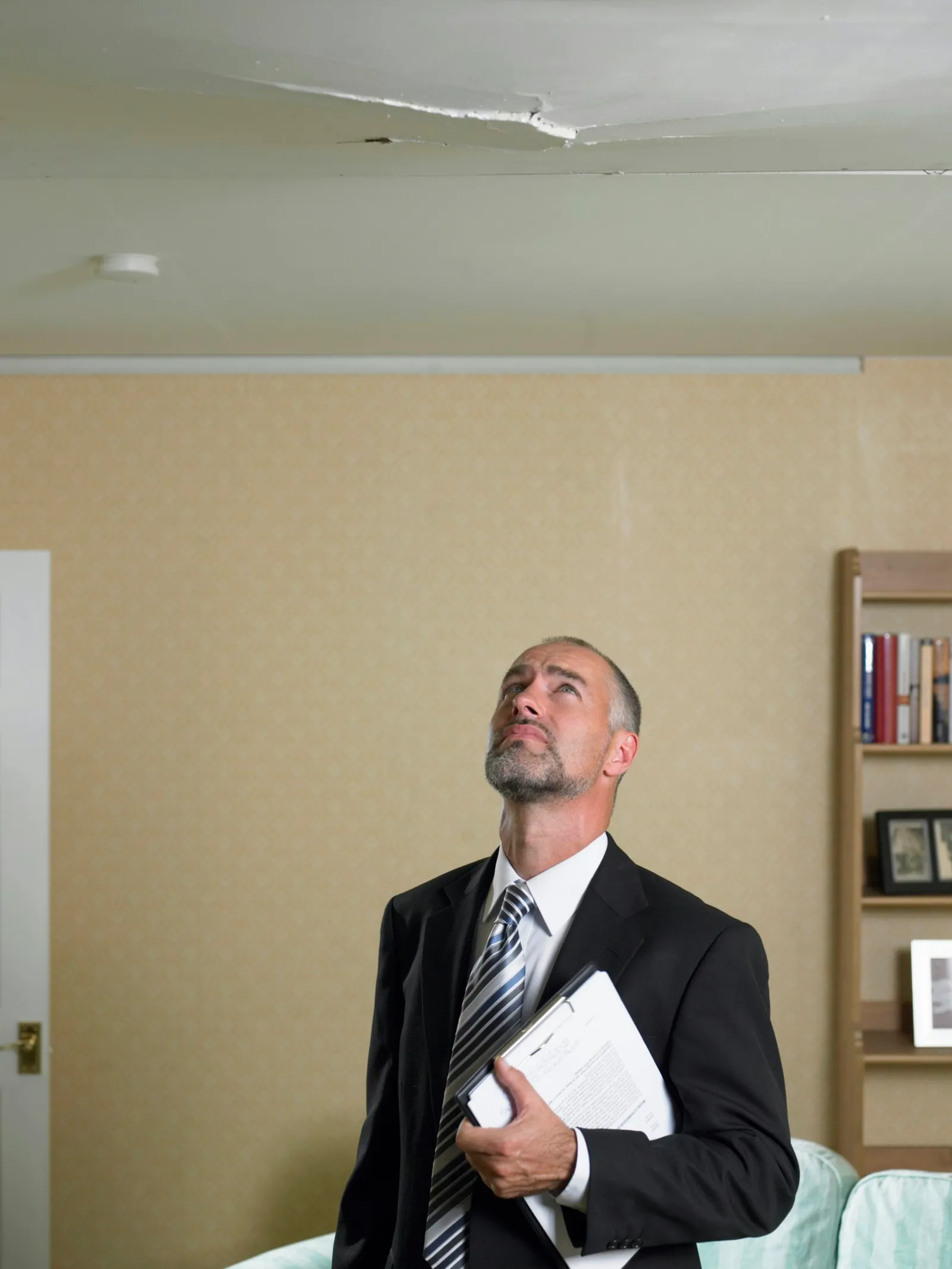 Mature man in suit with clipboard looking up at crack in ceiling