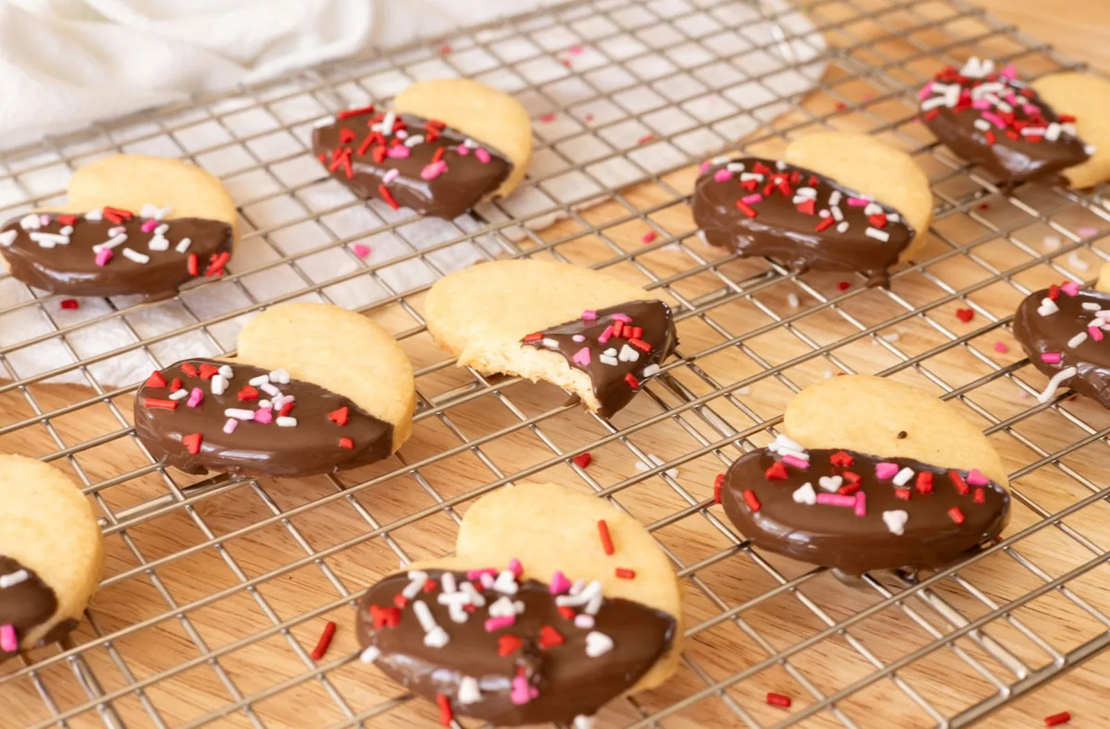 Heart-shaped shortbread cookies dipped in chocolate, arranged on a wire rack.