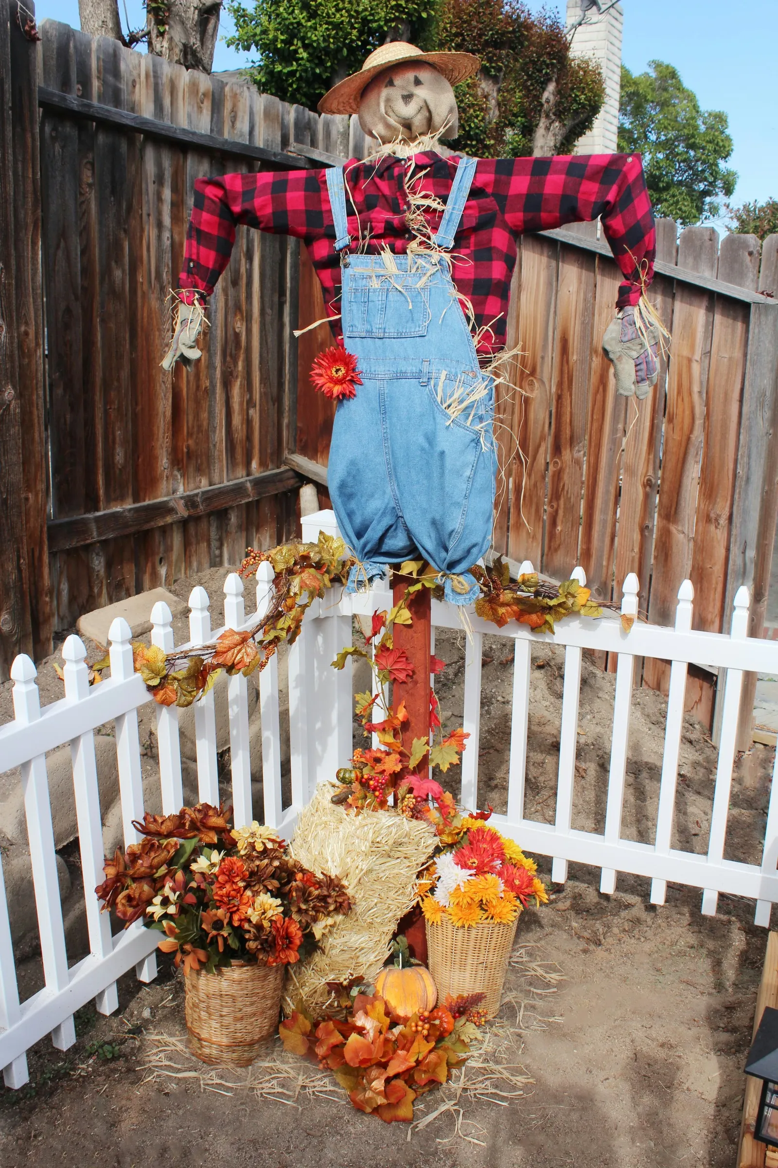 scarecrow on a sign post in a garden surrounded by autumn decor