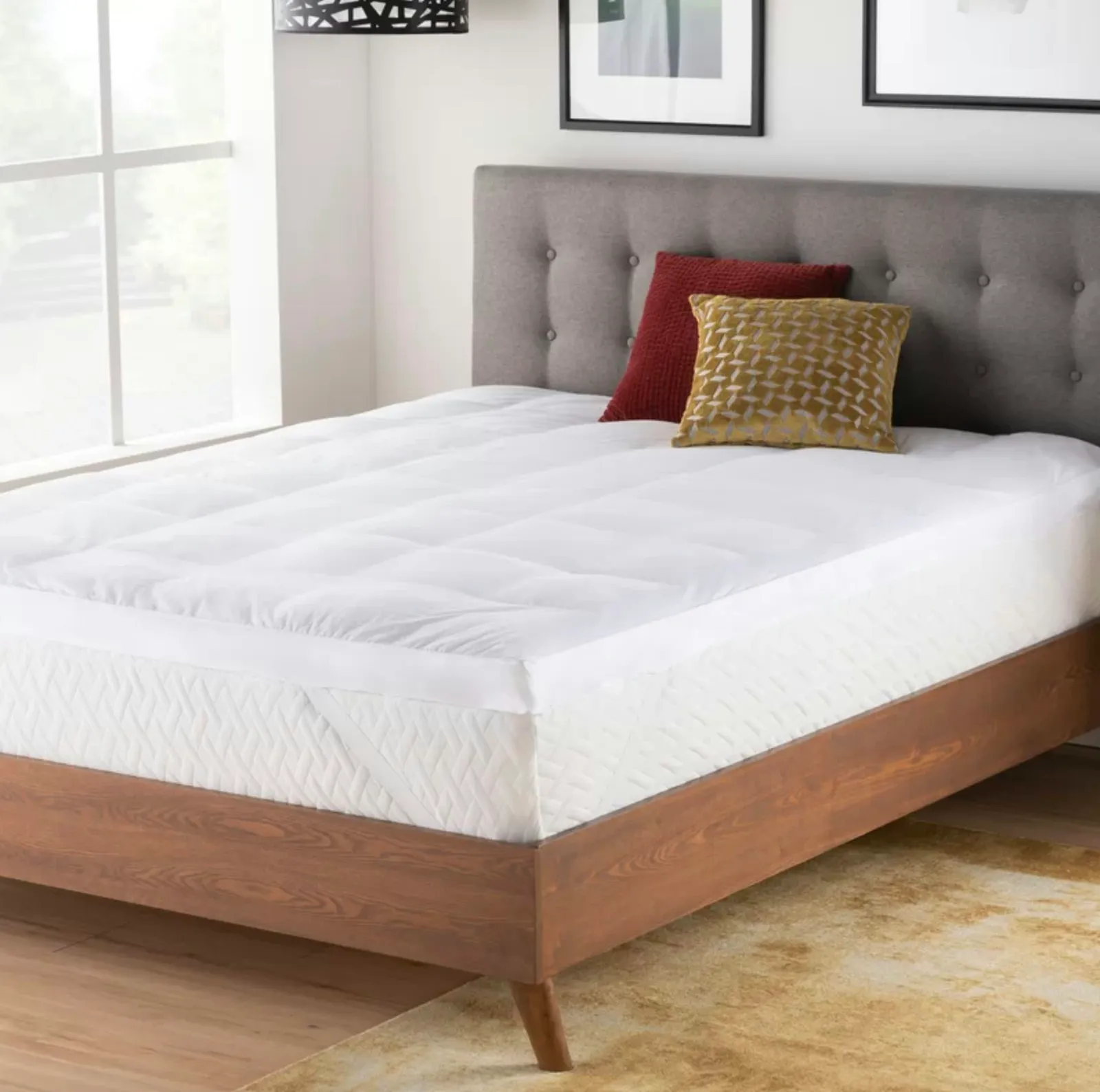White mattress topper on wood bed frame with a gray tufted headboard. The topper is 3 inches thick and quite fluffy looking.