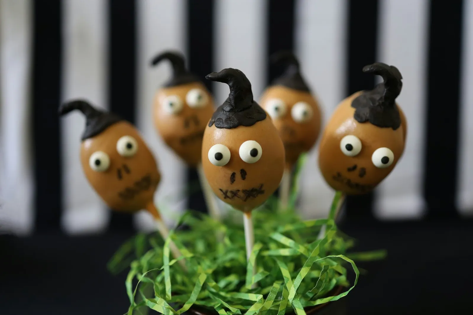 "Beetlejuice" shrunken head cake pops displayed in a jar with green paper grass