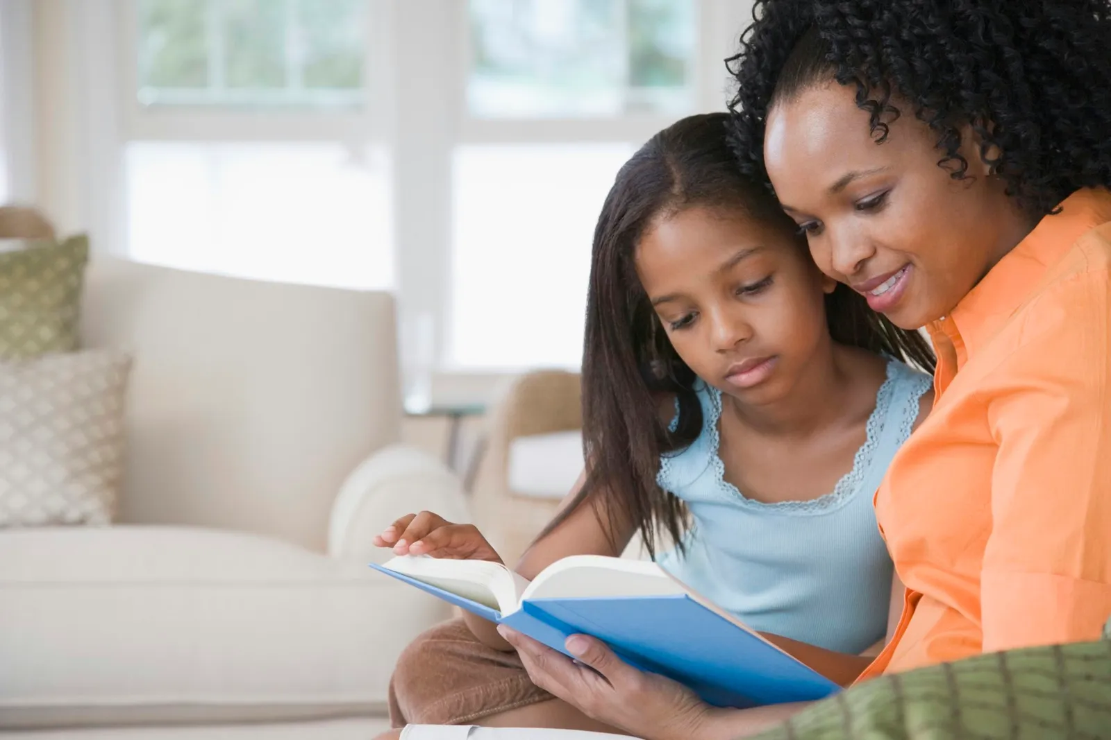 Side profile of a mid adult woman reading a book with her daughter and smiling