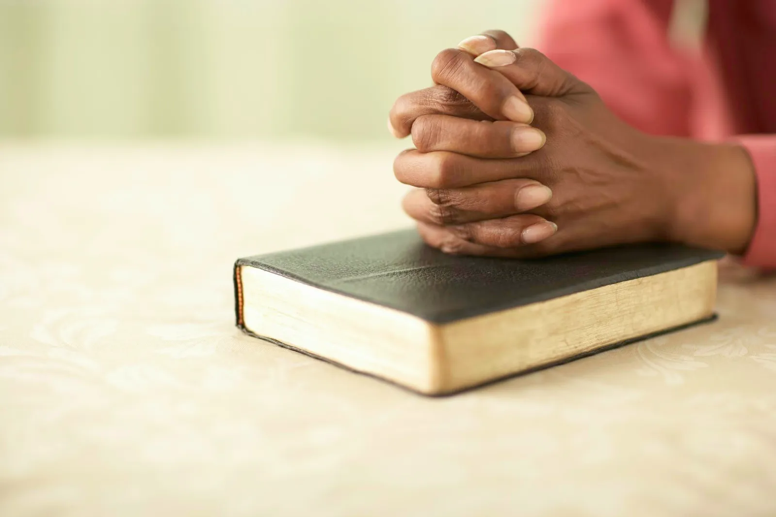 Senior woman sitting at table with hands clasped on Bible, close-up of hands